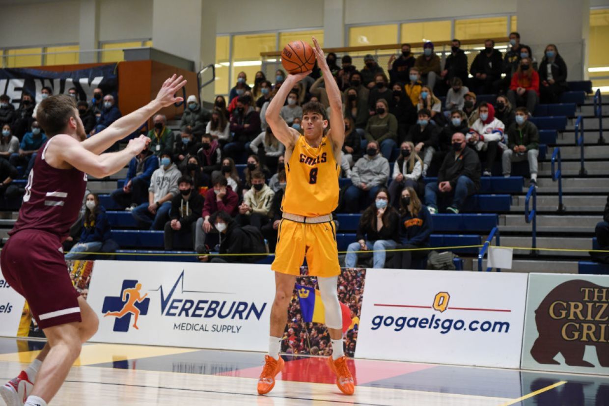 A member of the men's basketball team jump and throws the ball.