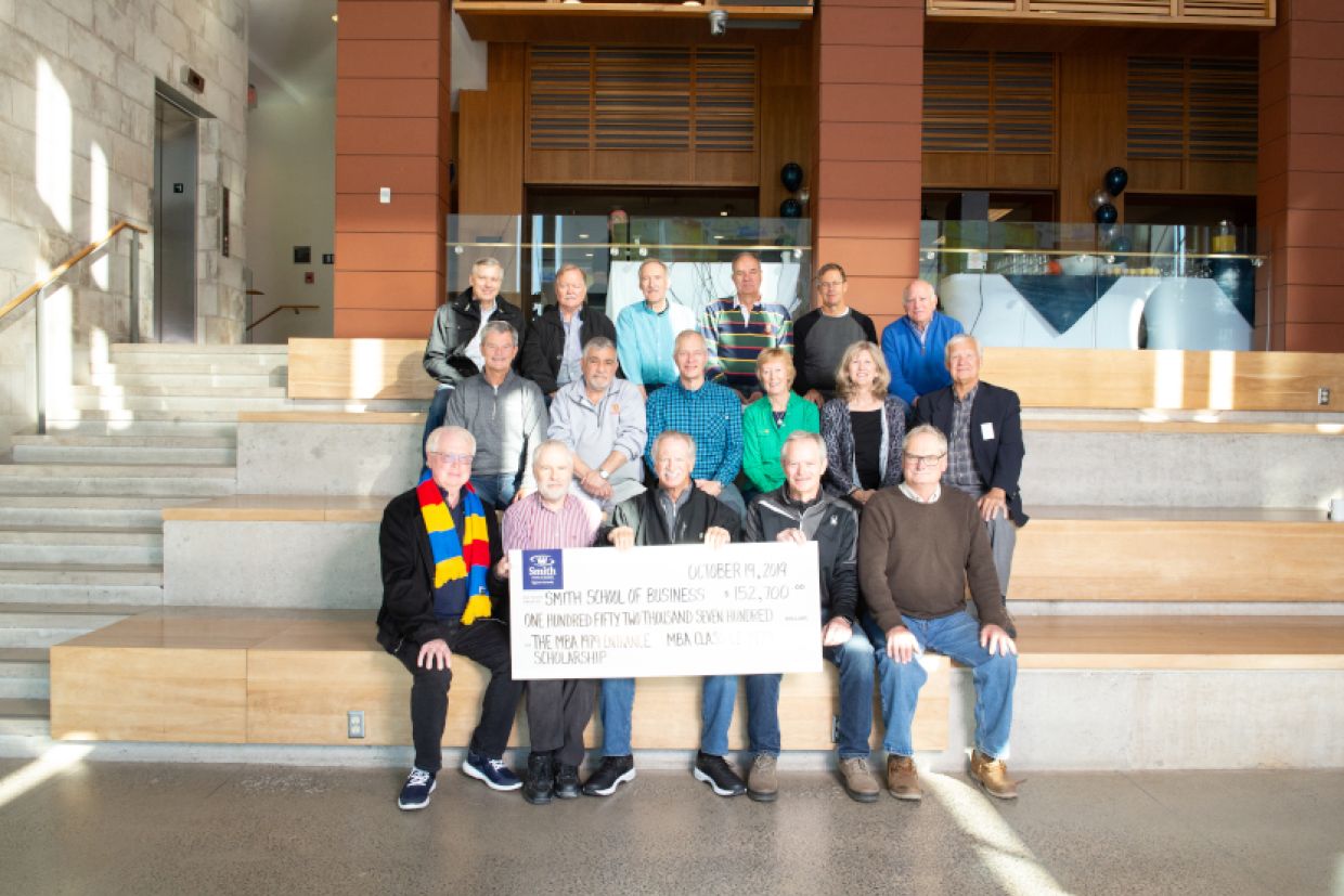 MBA'79 sitting in Goodes Hall holding their fundraising cheque