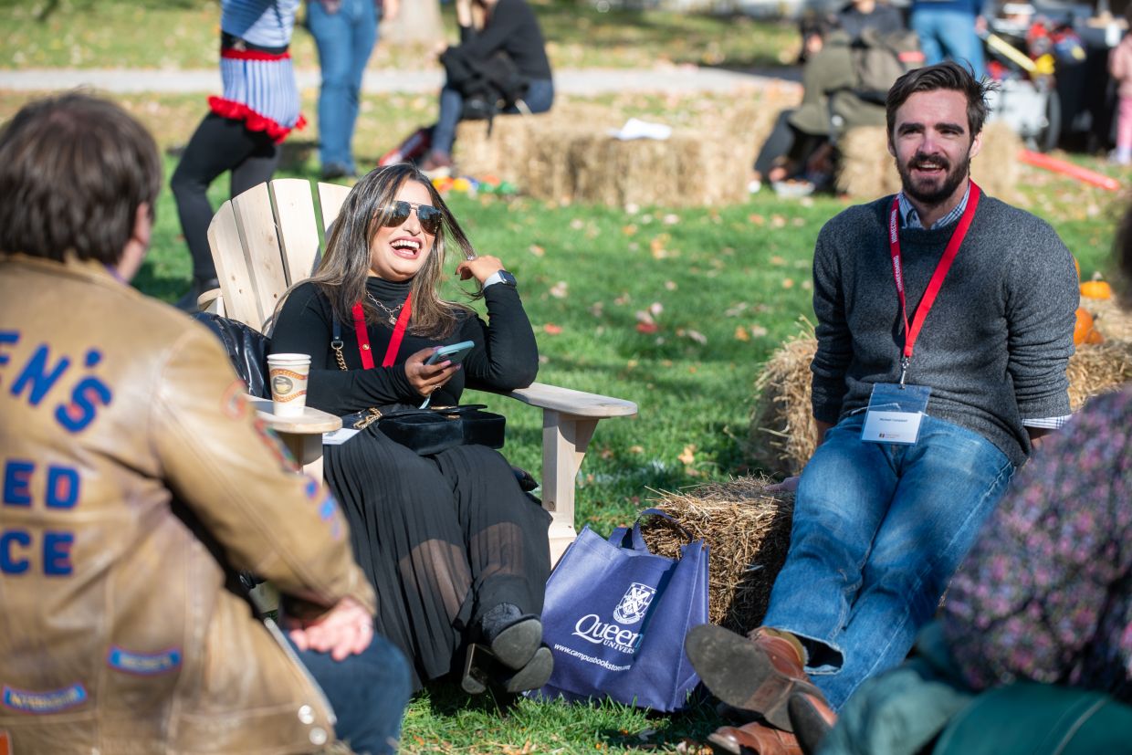 Alumni seated, laughing and smiling as they socialize outside.