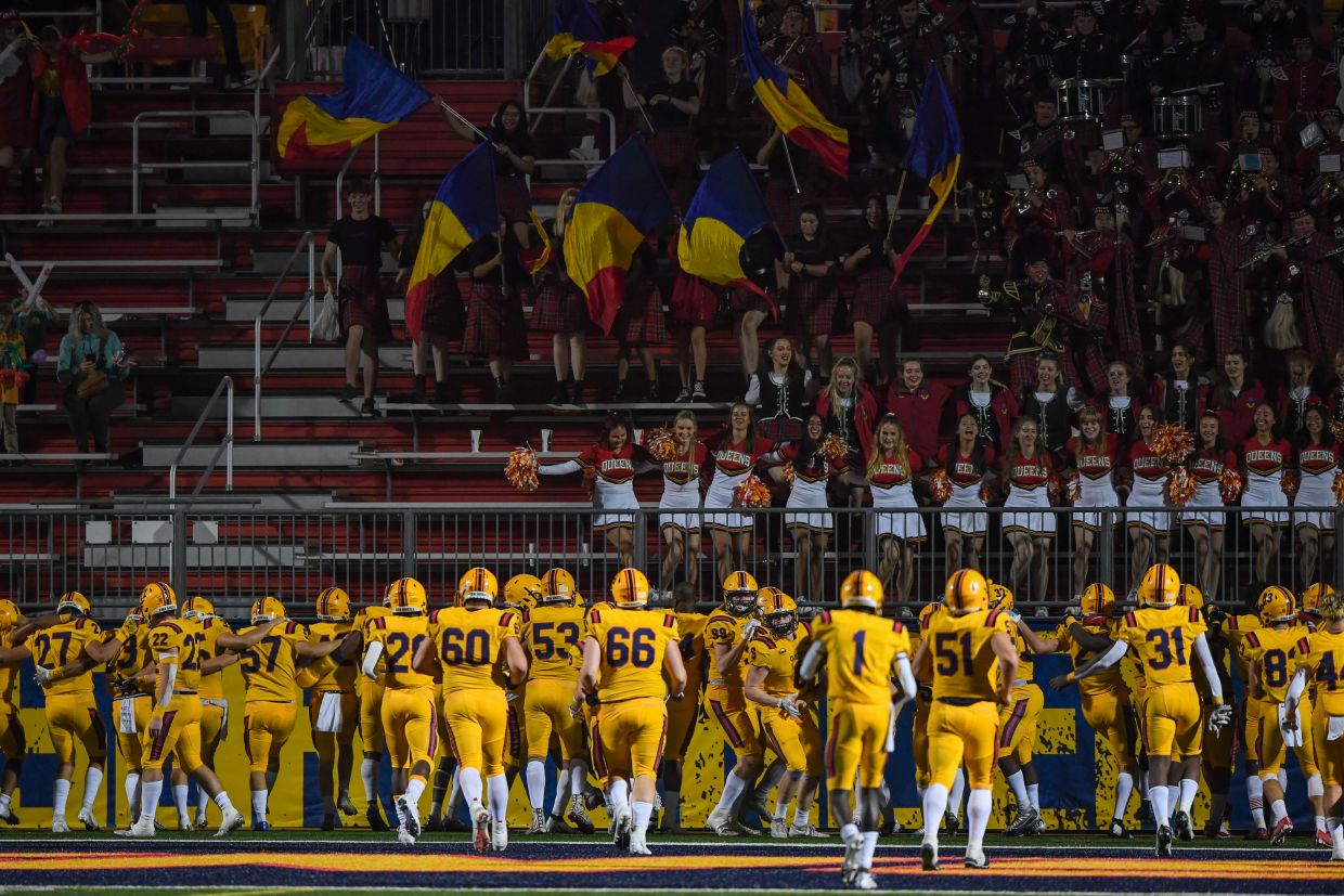 Football team celebrating with Queen's Flags and bands cheer team in the background