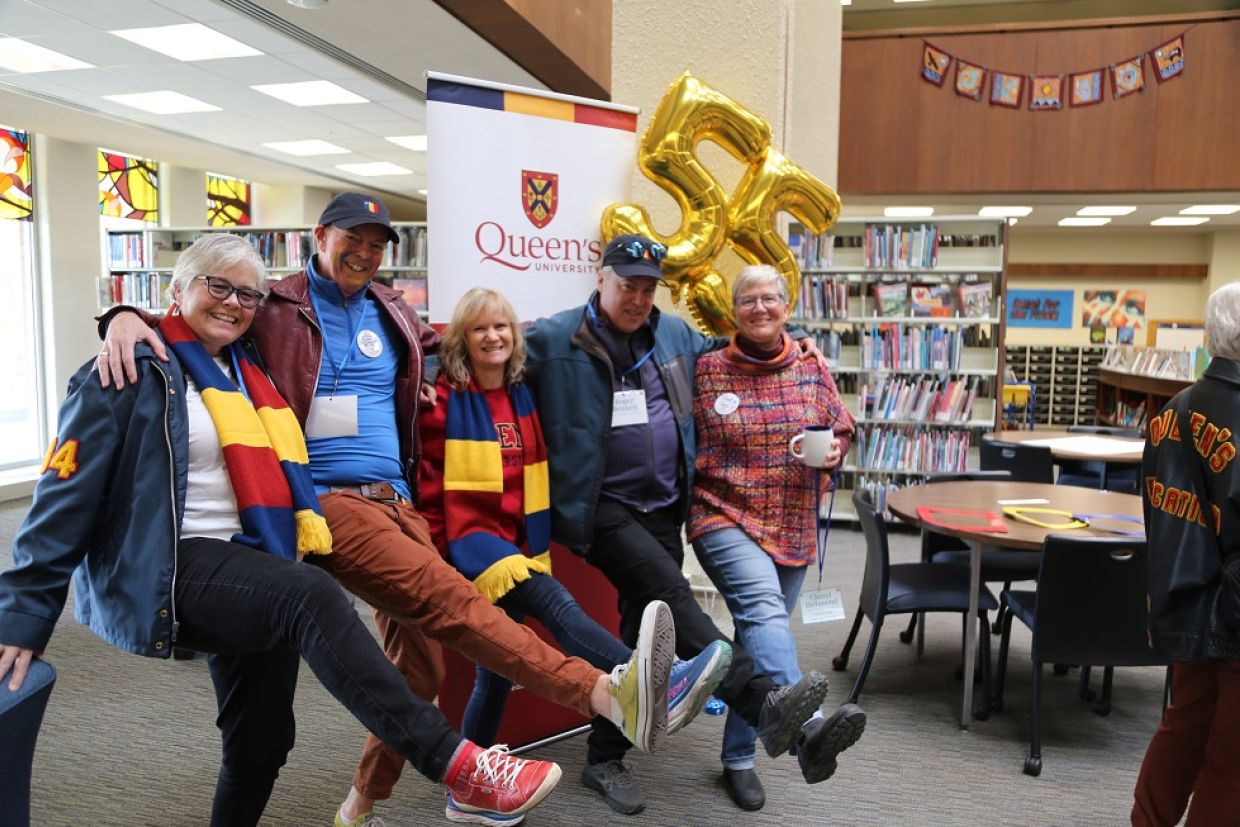 A group of alumni do a kick line in the library