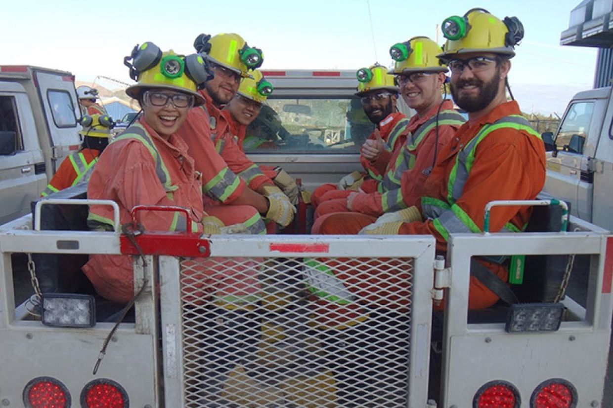 A group of students in mining safety equipment smile in the back of a truck