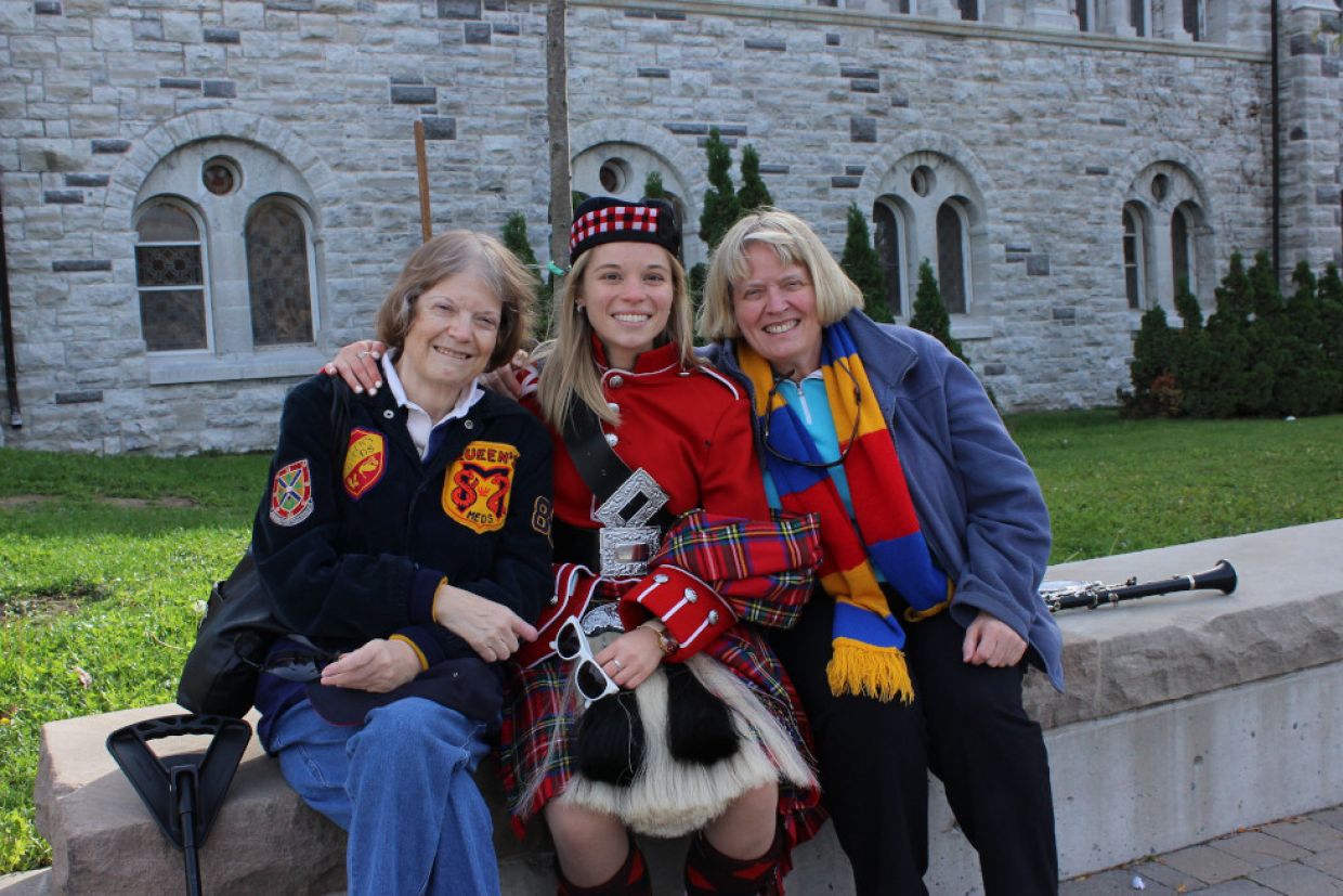 A student dressed in Queen's Band uniform, sits with her mother and grandmother on either side. 