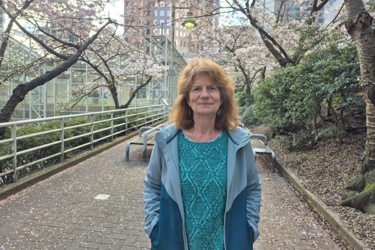 Annette Wilde, Artsci’80, stands in front of a flowering tree, smiling and enjoying the vibrant spring scenery.