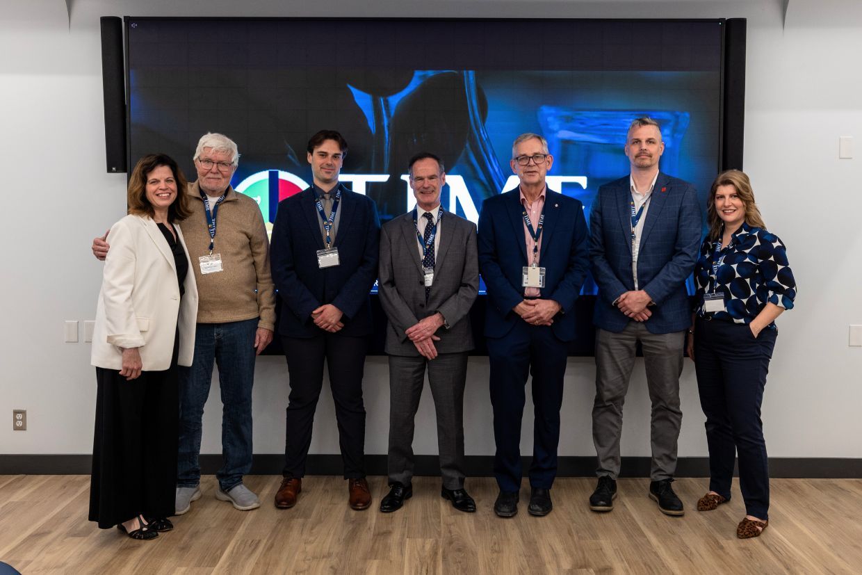 A diverse group of individuals stands before a large screen, highlighting the new W.J. Henderson TIME Collaboratory initiative at Queen’s.