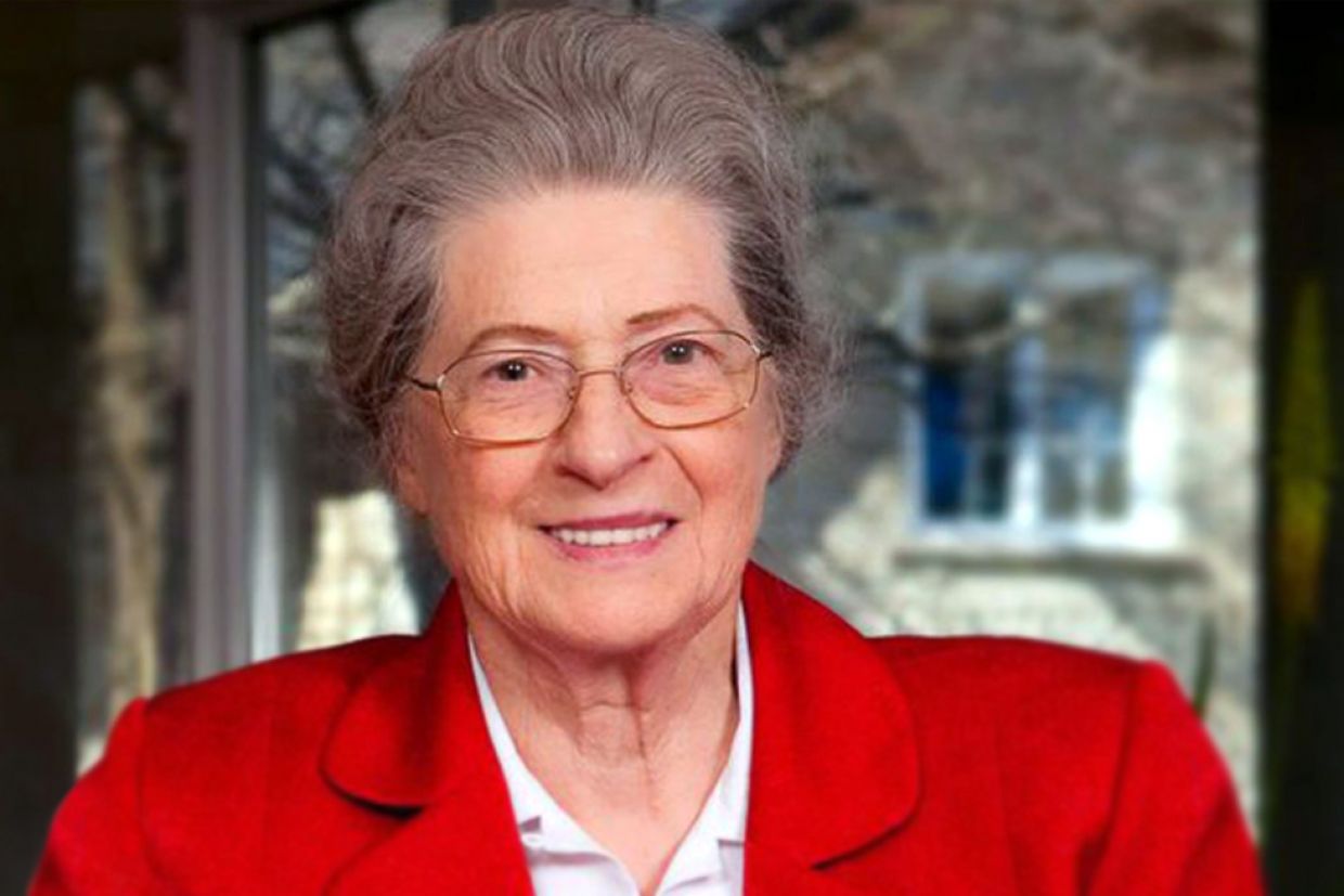 Isabel Bader in a red collared shirt and glasses, smiles at the camera.