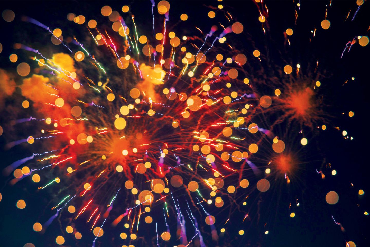 Photo of fireworks in blue, red, and yellow with bokeh
