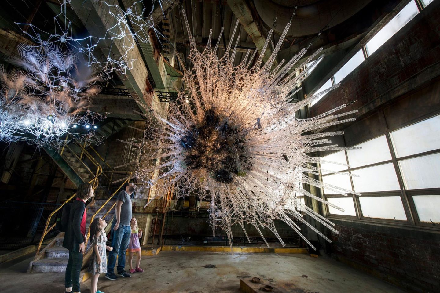 A group of people stands before a large, intricate sculpture, showcasing Philip Beesley's immersive art installation.