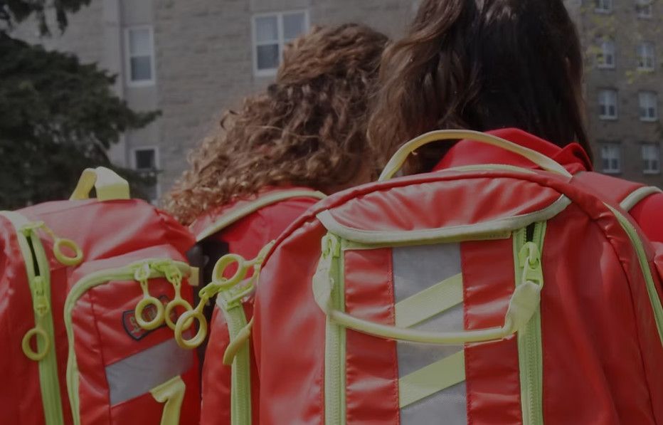 Two QFA volunteers with their bright orange backpacks on, backs to camera, facing Vic Hall