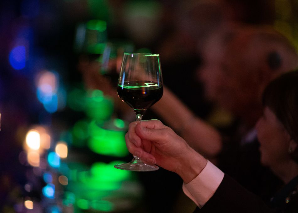 Glass of red wine being held up as a toast in a dark bar setting