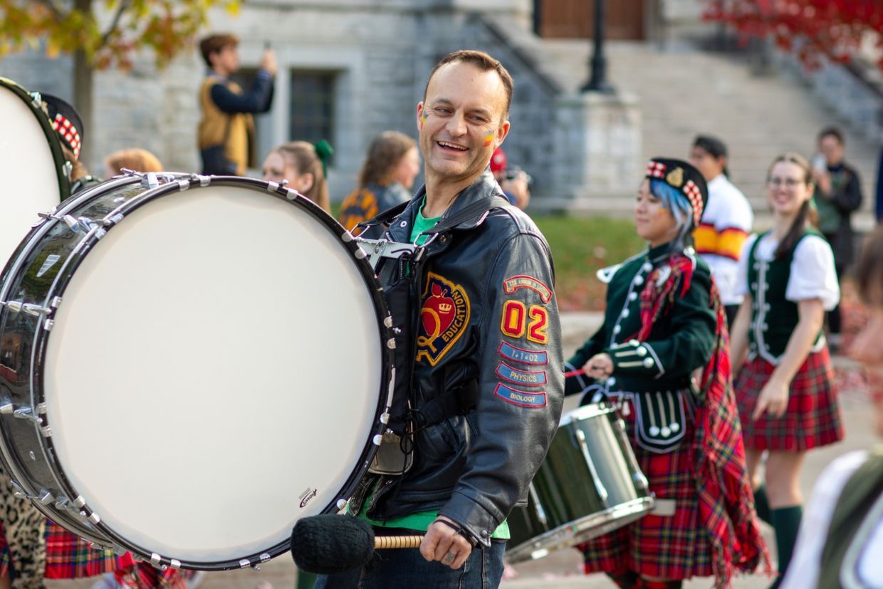 A man dressed in a kilt holds a drum, representing the festive spirit of Homecoming's 100th anniversary.