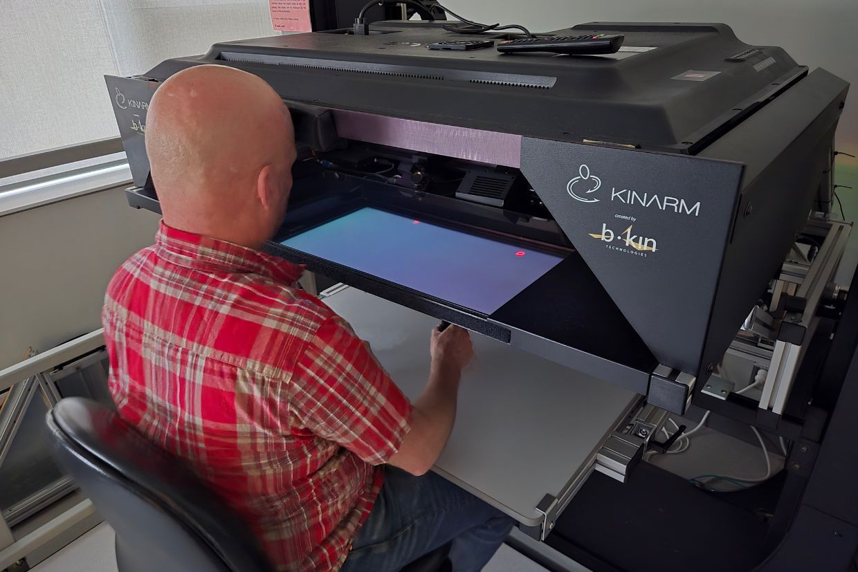 A man operates a device connected to a computer, showcasing innovative research in neurological and mobility sciences.