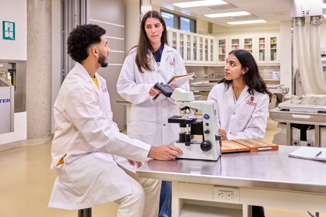 Three medical students in lab coats engaged in a discussion, showcasing collaboration and teamwork in a clinical setting.