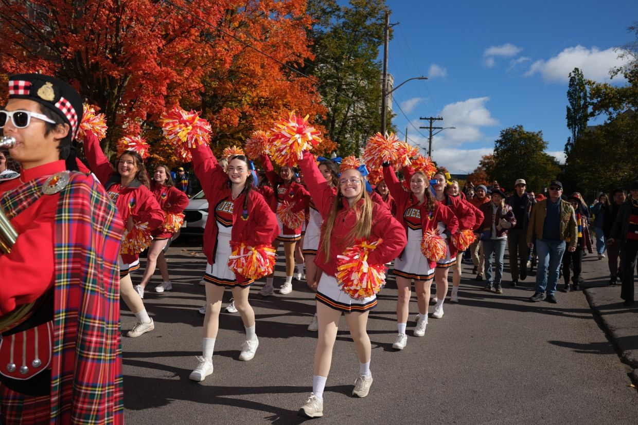 A group of alumni, cheerleaders, and band members in red and white walking together during the Homecoming 100 parade.
