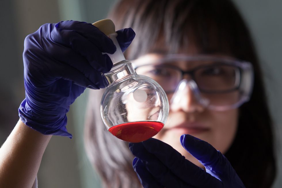 Person holds up a scientific beaker, analyzing the red liquid inside.