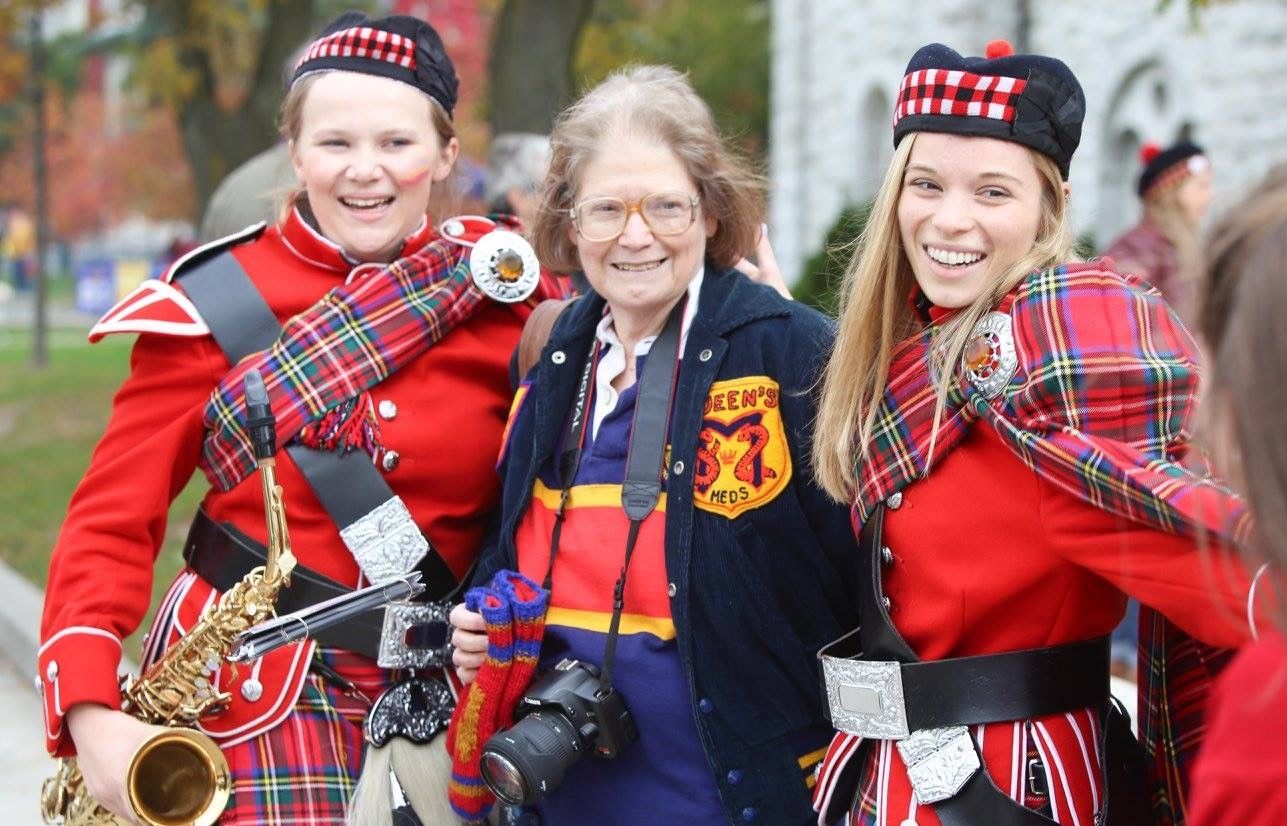 Dr. Pamela Frid posing at Homecoming between two members of Queen's Bands. 