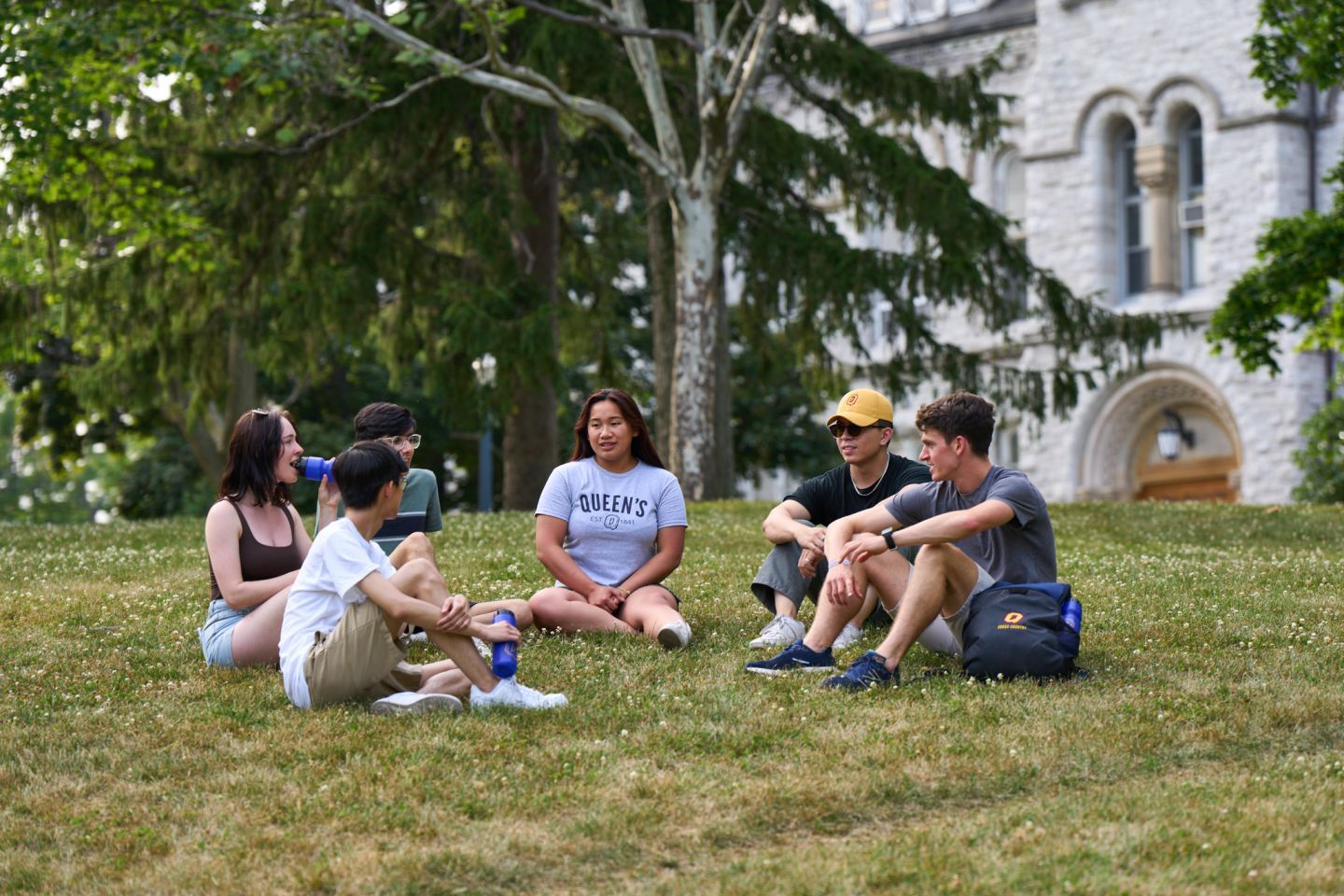 Group of students sitting and chatting on the lawn in front of Theological Hall