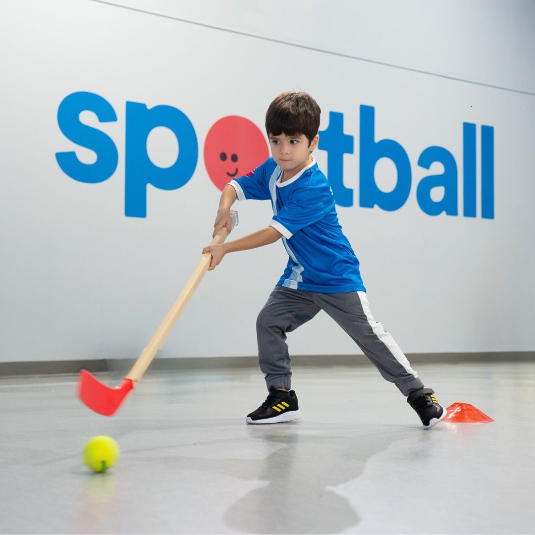 Child stickhandling a ball in front of Sportball decal. 