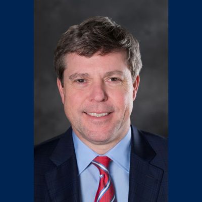 Toby smiling and wearing a blue shirt and jacket with a red tie.