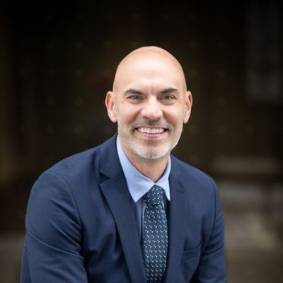 Gareth smiling wearing a blue suit, shirt and tie 