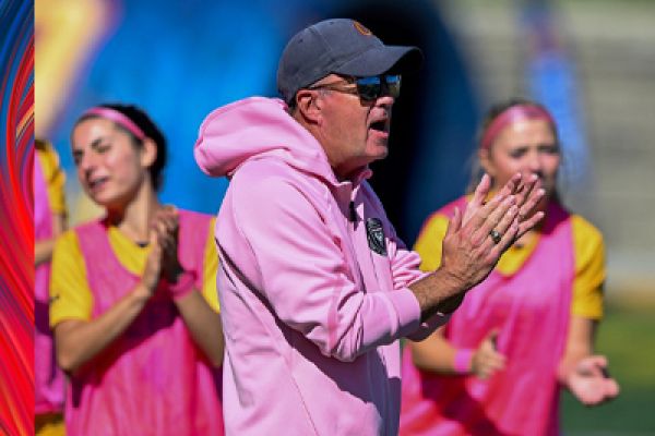 photo of David McDowell, clapping hands. Wearing a blue cap and pink sweatshirt. Individuals in background wearing pink and yellow