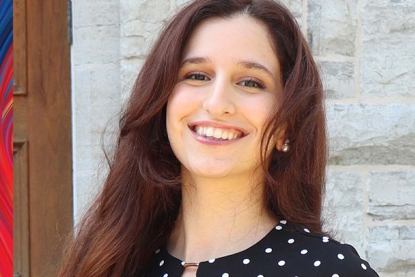 Natalie Kearn in front of a grey wall smiling, wearing a black shirt with white dots