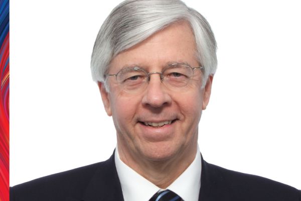 David Nesbitt smiling wearing a black suit jacket, white shirt, black tie and glasses