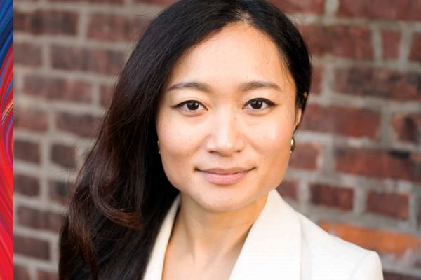 Diana Chang in front of a brick wall, wearing a white suit jacket, with long hair