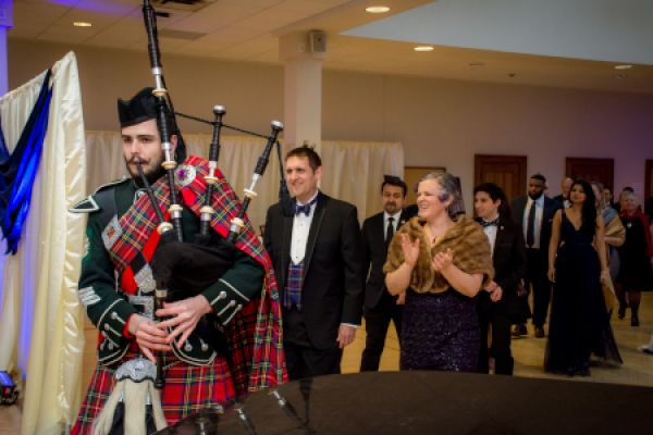 A person in a kilt plays bag pipes and leads award winners into a hall.