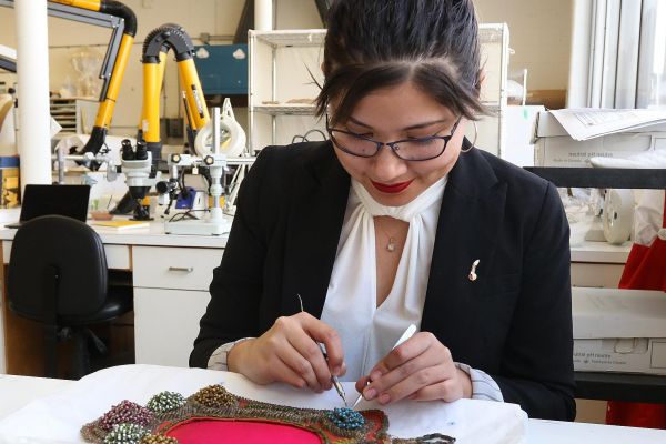 A woman in a lab meticulously crafting a piece of jewelry, showcasing her skills in art conservation. Credit: Bernard Clark