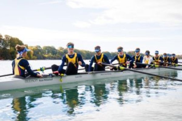 Rowing team in action, following their captain, and with a beautiful lake setting as a background.