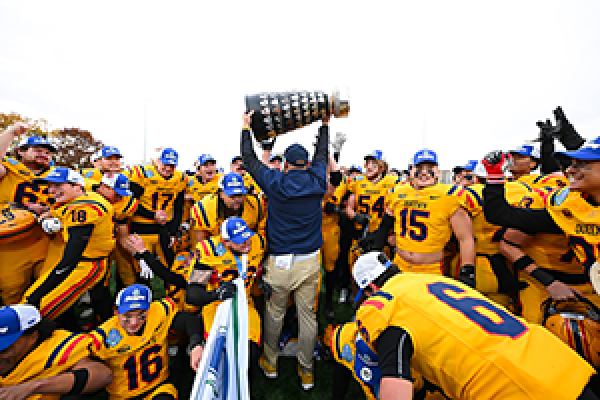 Coach Steve Snyder hoisting the Yates Cup surrounded by Queen's Football players
