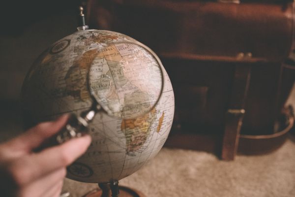A globe sits on a desk, while a magnifying glass is held above it.