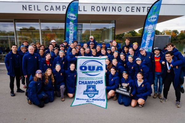The rowing team from Ontario University Athletics stands together for a photo in front of their building, showcasing team spirit.