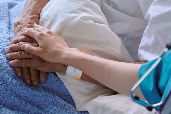 A medical care professional gently holds the hand of an elderly person, providing comfort and support in a caring environment.