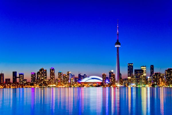 Toronto skyline at night featuring the CN Tower prominently illuminated in the foreground against a dark sky.
