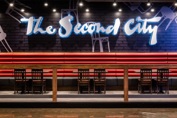 Interior shot of the Second City venue, chairs and tables beside the Second City sign on the wall.