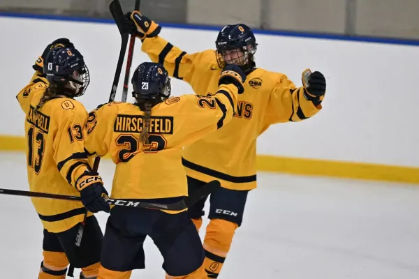 Three Queen's University Women's Hockey players celebrating together post-goal with arms in the air