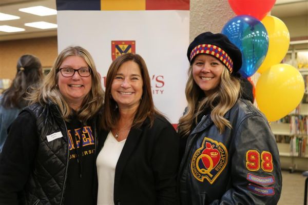 Three alumni stand in front of balloons smiling in the library
