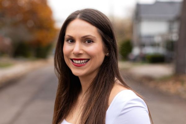 Ani Colekessian, Artsci’07, smiling to the camera wearing a white blouse and with trees and a street as the background. 