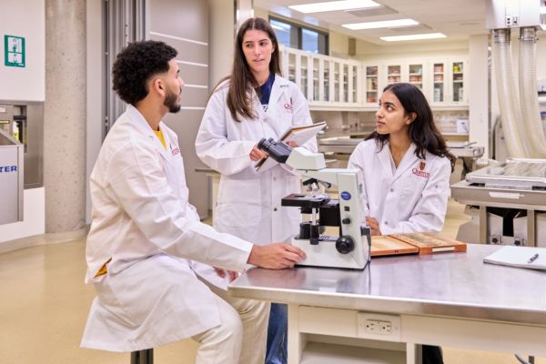 Three medical students in lab coats engaged in a discussion, showcasing collaboration and teamwork in a clinical setting.