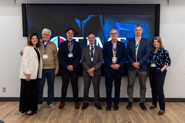 A diverse group of individuals stands before a large screen, highlighting the new W.J. Henderson TIME Collaboratory initiative at Queen’s.
