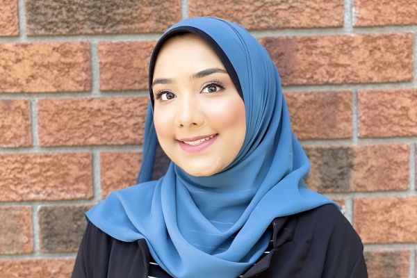 Headshot of Aelea Syed with a brick wall behind her. 