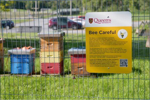 A "bee careful" sign on a fence around the apiary.