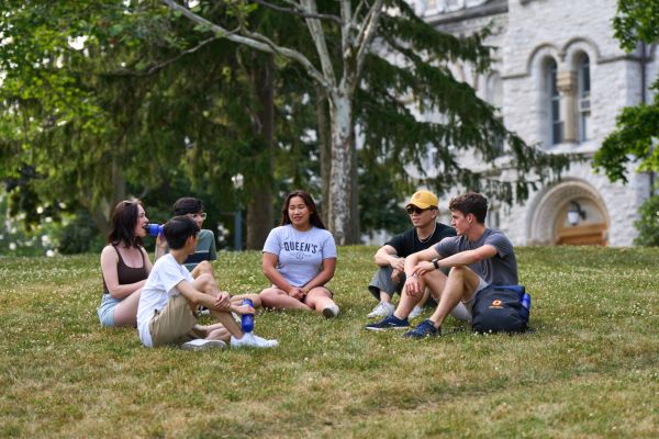 Group of students sitting and chatting on the lawn in front of Theological Hall