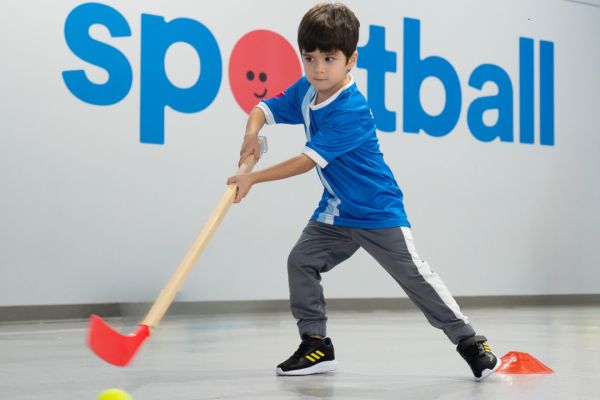 Child stickhandling a ball in front of Sportball decal. 