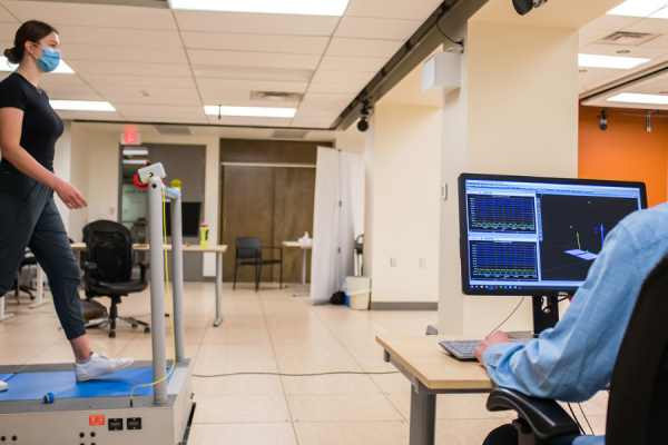 A test subject wearing a surgical mask walks on a treadmill as a second person views results on a computer screen