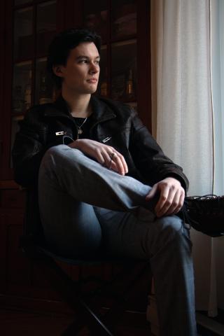 Photo of Lachlan McKinlay sitting in a chair with his leg crossed over the other, and looking out the window