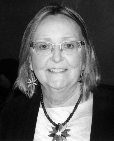 Black and white photo of Elizabeth McQuay – should-length hair, wearing glasses and beaded necklace.
