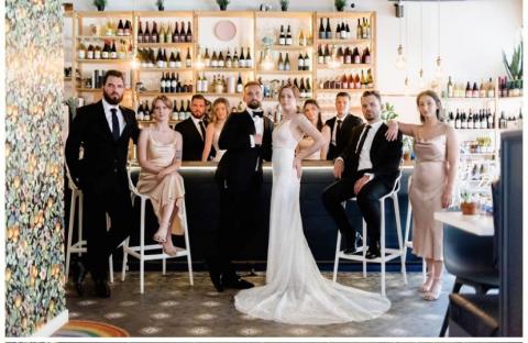 Formal photograph of a wedding party in from of a bar.